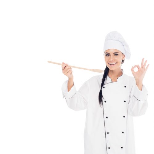 Smiling chef in uniform holding wooden spatula and showing okay sign isolated on white